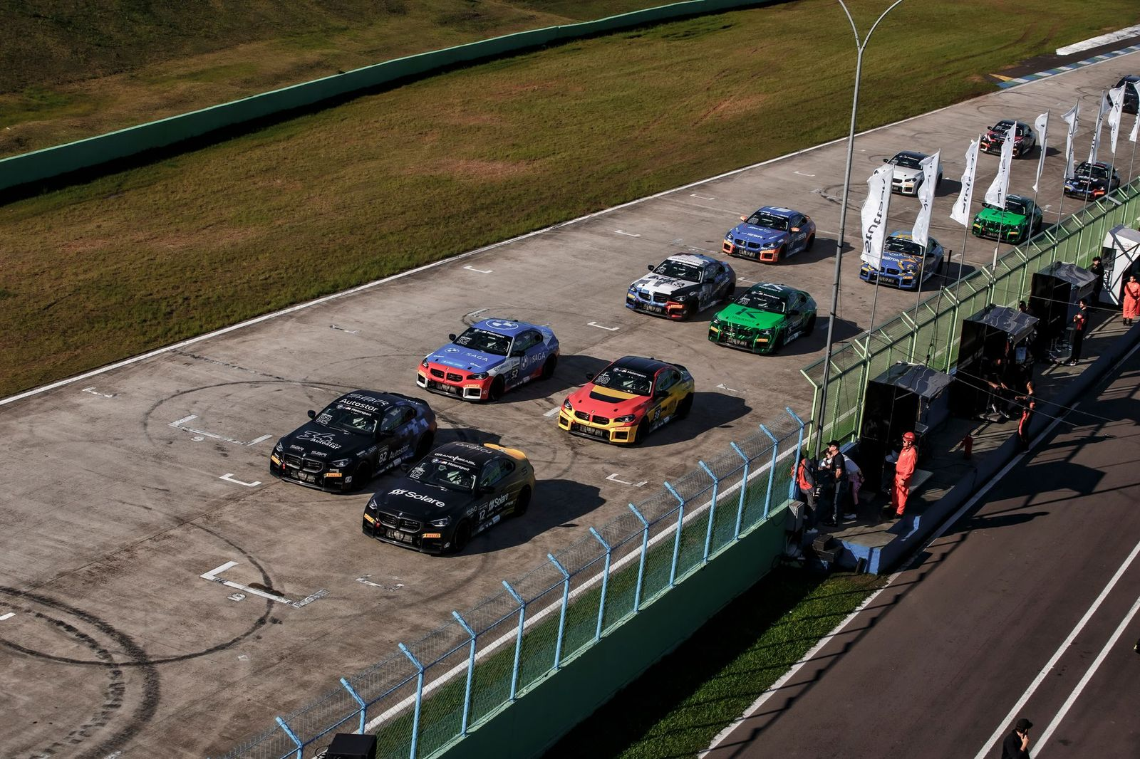Race cars aligned in the pit lane, with track personnel alongside.